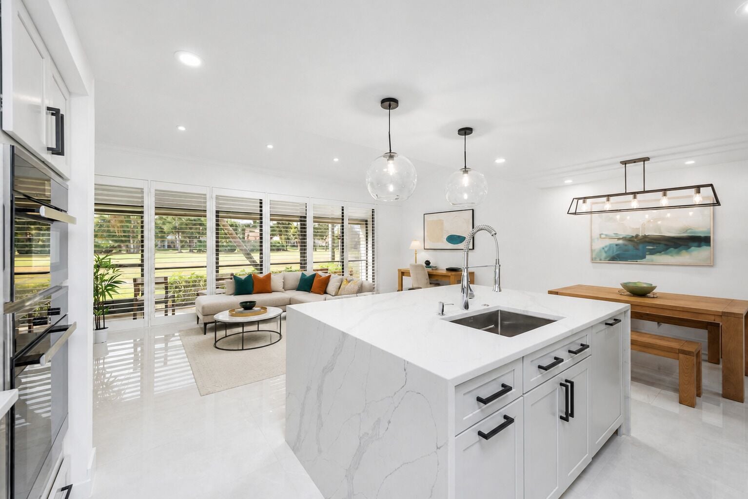 Una cocina moderna con una isla de mármol, electrodomésticos de acero inoxidable y un comedor con mesa y banco de madera.