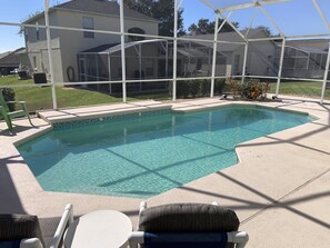 Ein klarer Pool mit gefliestem Rand, umgeben von einer überdachten Terrasse mit Stühlen und einem Tisch.