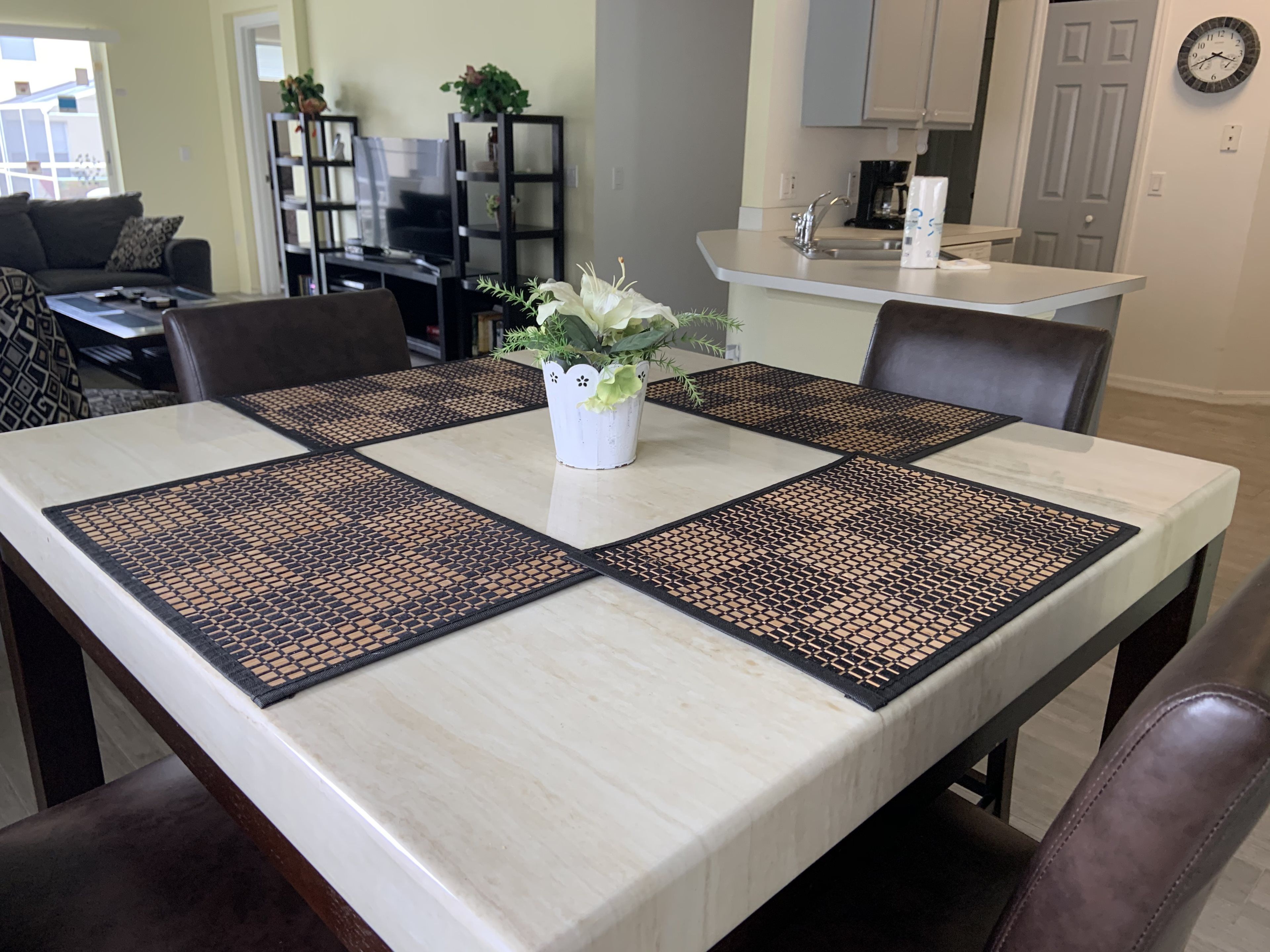 A dining table with four placemats, a vase with flowers, and a kitchen in the background.