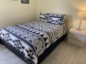 A bed with a black and white patterned bedspread and pillows, a bedside table with a lamp, and a light-colored wall.