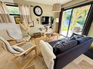 Un salon avec un canapé, des fauteuils, un téléviseur et une horloge au mur.