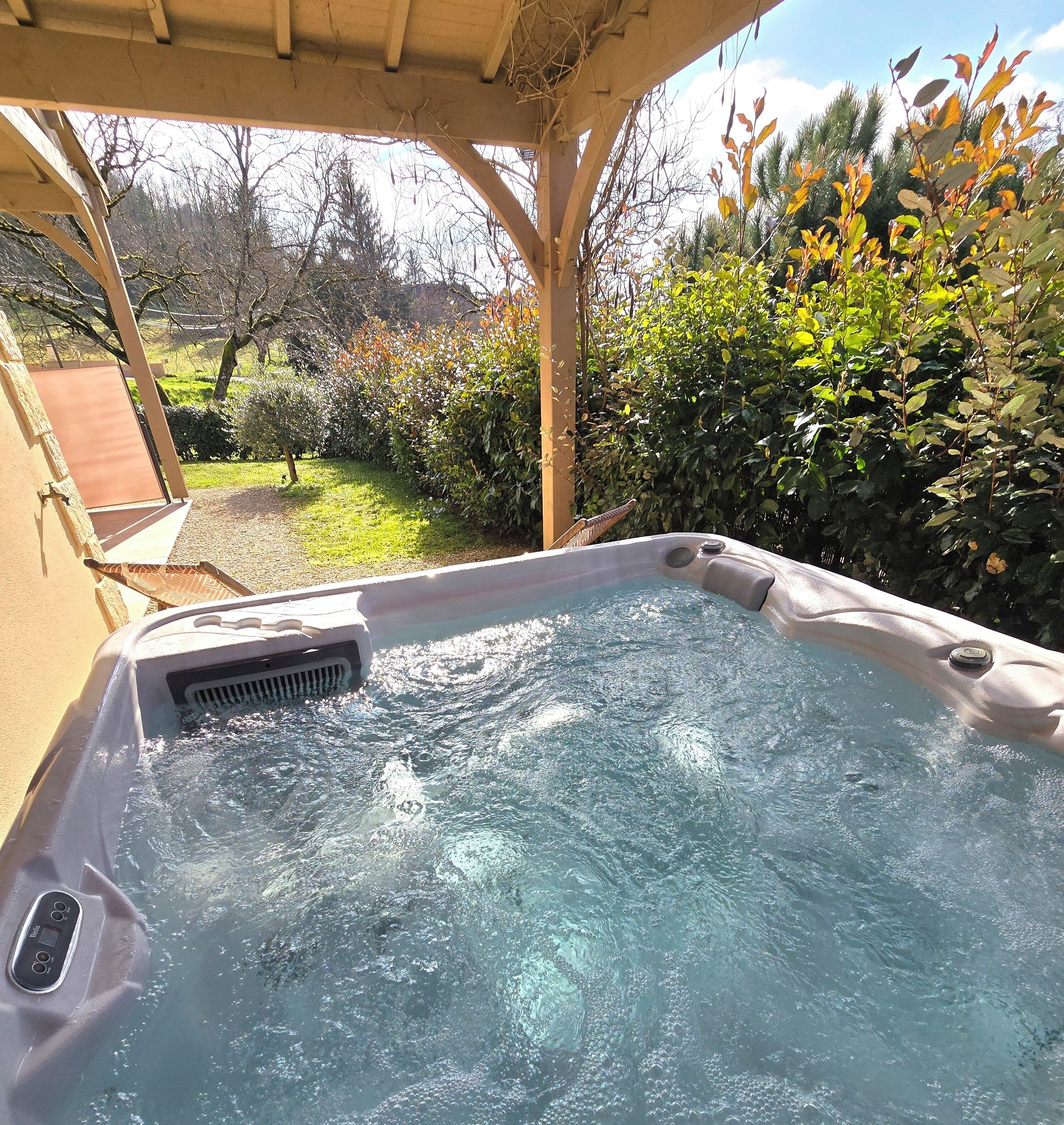A hot tub with a control panel, surrounded by a garden with various plants and trees.