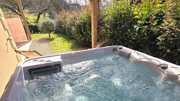A hot tub with a control panel, surrounded by a garden with various plants and trees.