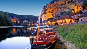 A boat docked at a riverside location with a building in the background. - LOU MIYA - Gîte Périgourdin 5kms from SARLAT, Air conditioning, Jacuzzi SPA WELLIS (Carsac-Aillac)