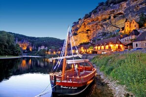 A boat docked at a riverside location with a building in the background. - LOU MIYA - Gîte Périgourdin 5kms from SARLAT, Air conditioning, Jacuzzi SPA WELLIS (Carsac-Aillac)