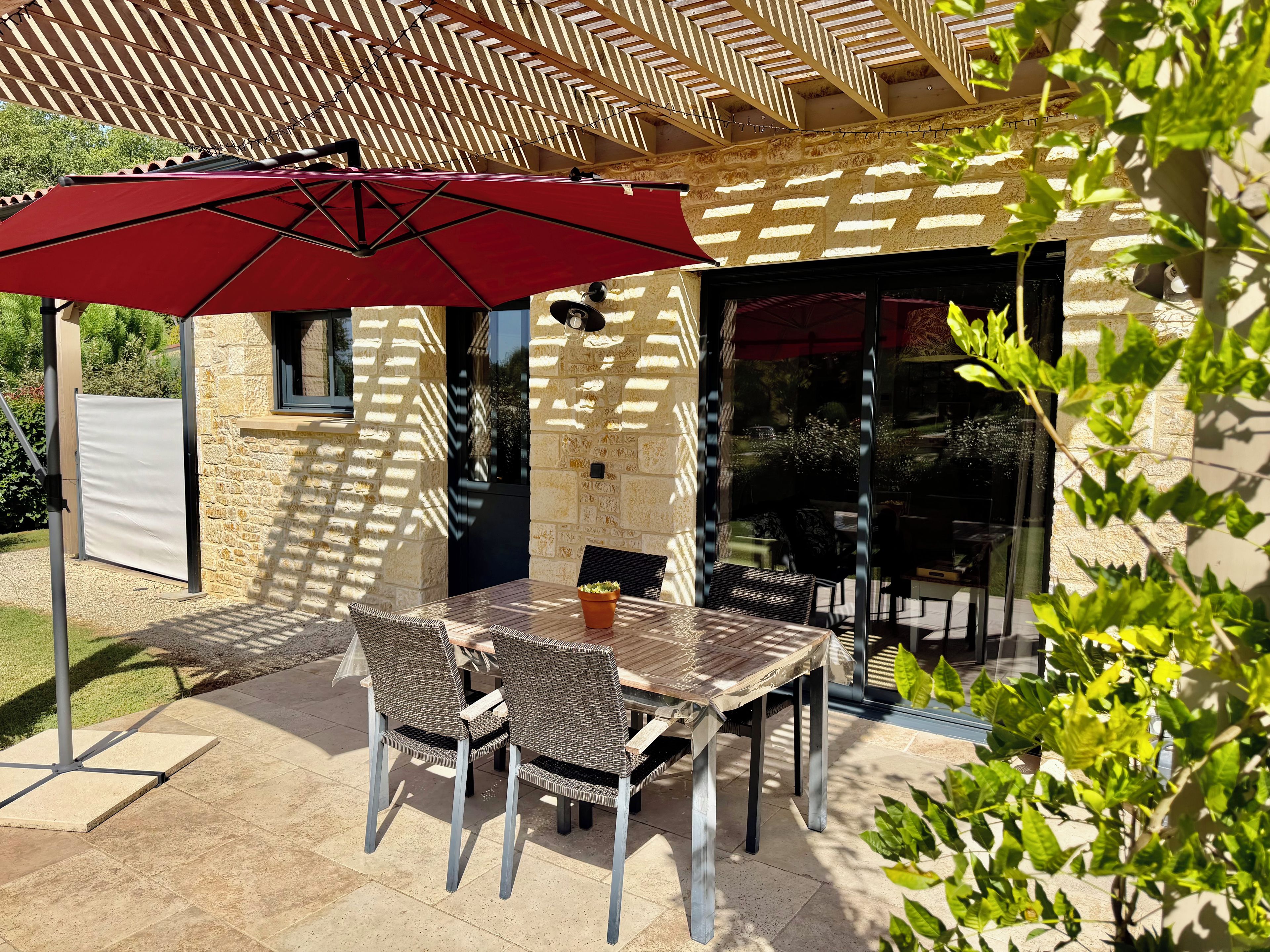 An outdoor patio with a table and chairs, a red umbrella, and a stone wall.