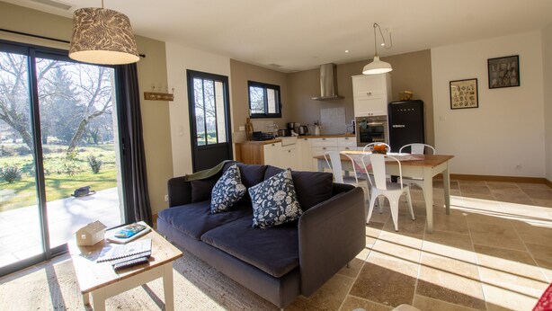 Una sala de estar moderna con un sofá oscuro, una mesita y vistas a un jardín a través de amplios ventanales.