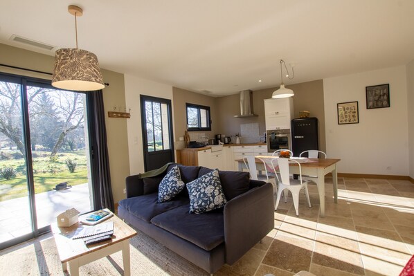 A modern living room with a dark sofa, a small table, and a view of a garden through large windows. - LOU MIYA - Gîte Périgourdin 5kms from SARLAT, Air conditioning, Jacuzzi SPA WELLIS (Carsac-Aillac)