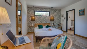 Un dormitorio con una cama, un ordenador portátil sobre un escritorio, un espejo y una ventana.