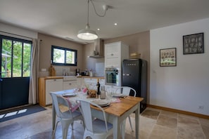 A modern kitchen with white cabinets, a wooden dining table, and a black refrigerator. - LOU MIYA - Gîte Périgourdin 5kms from SARLAT, Air conditioning, Jacuzzi SPA WELLIS (Carsac-Aillac)