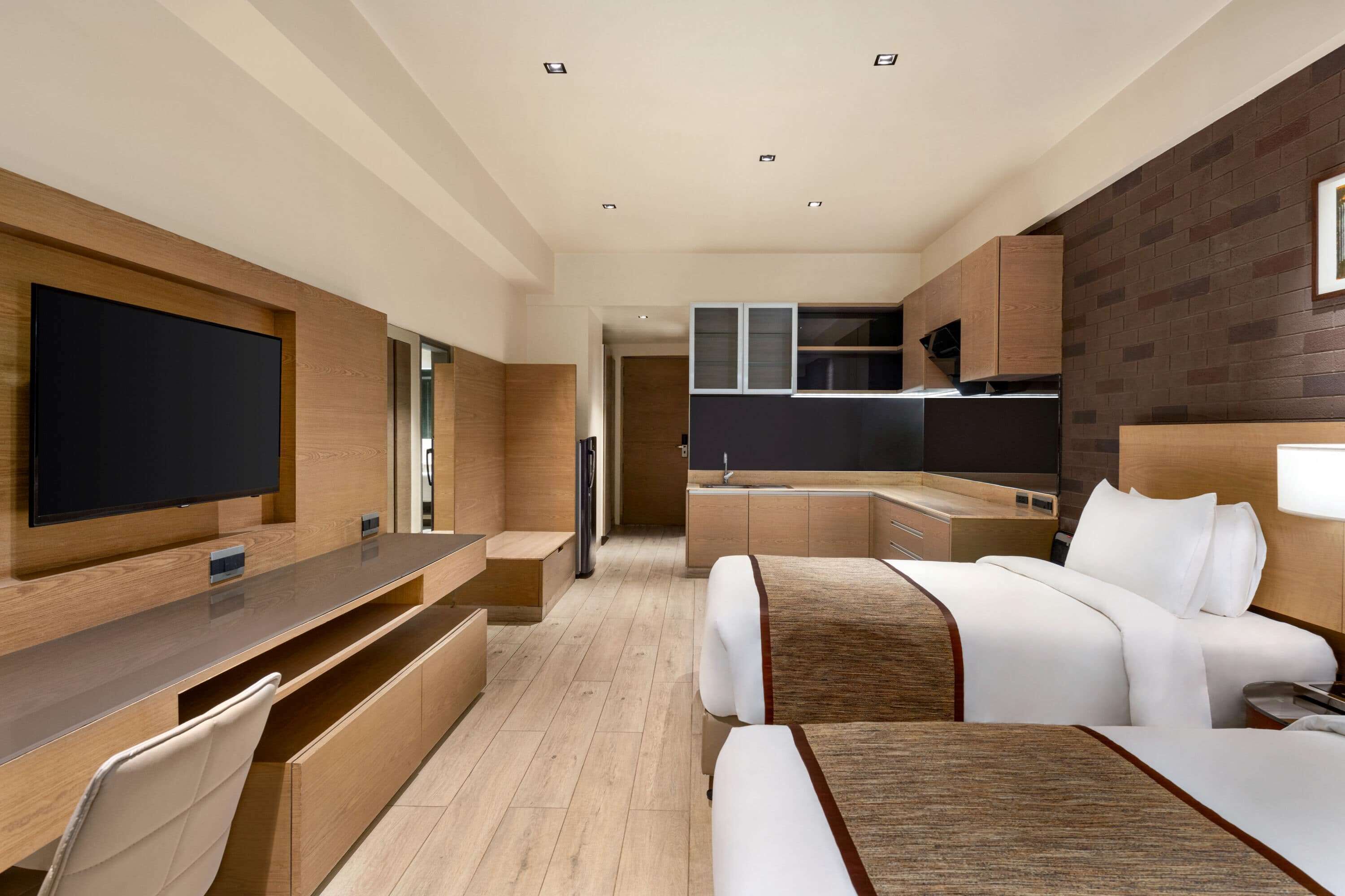 A modern hotel room with a flat-screen TV, a sofa, a bed, a desk, and a kitchenette.
