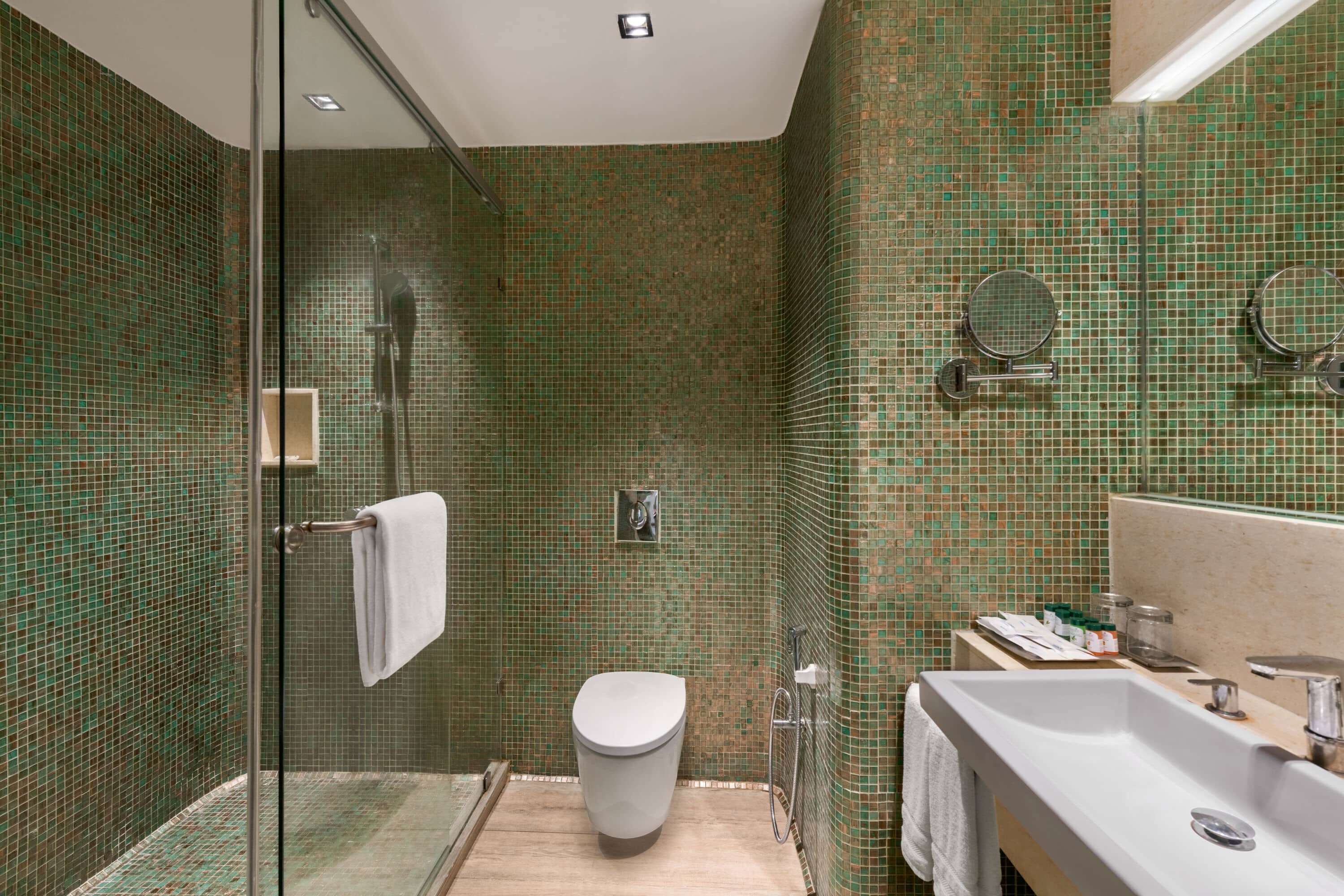 A bathroom with a glass shower enclosure, a toilet, and a sink with a mirror.