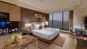 Una habitación de hotel moderna con cama, escritorio, silla, televisor, ventana grande y zona de cocina.