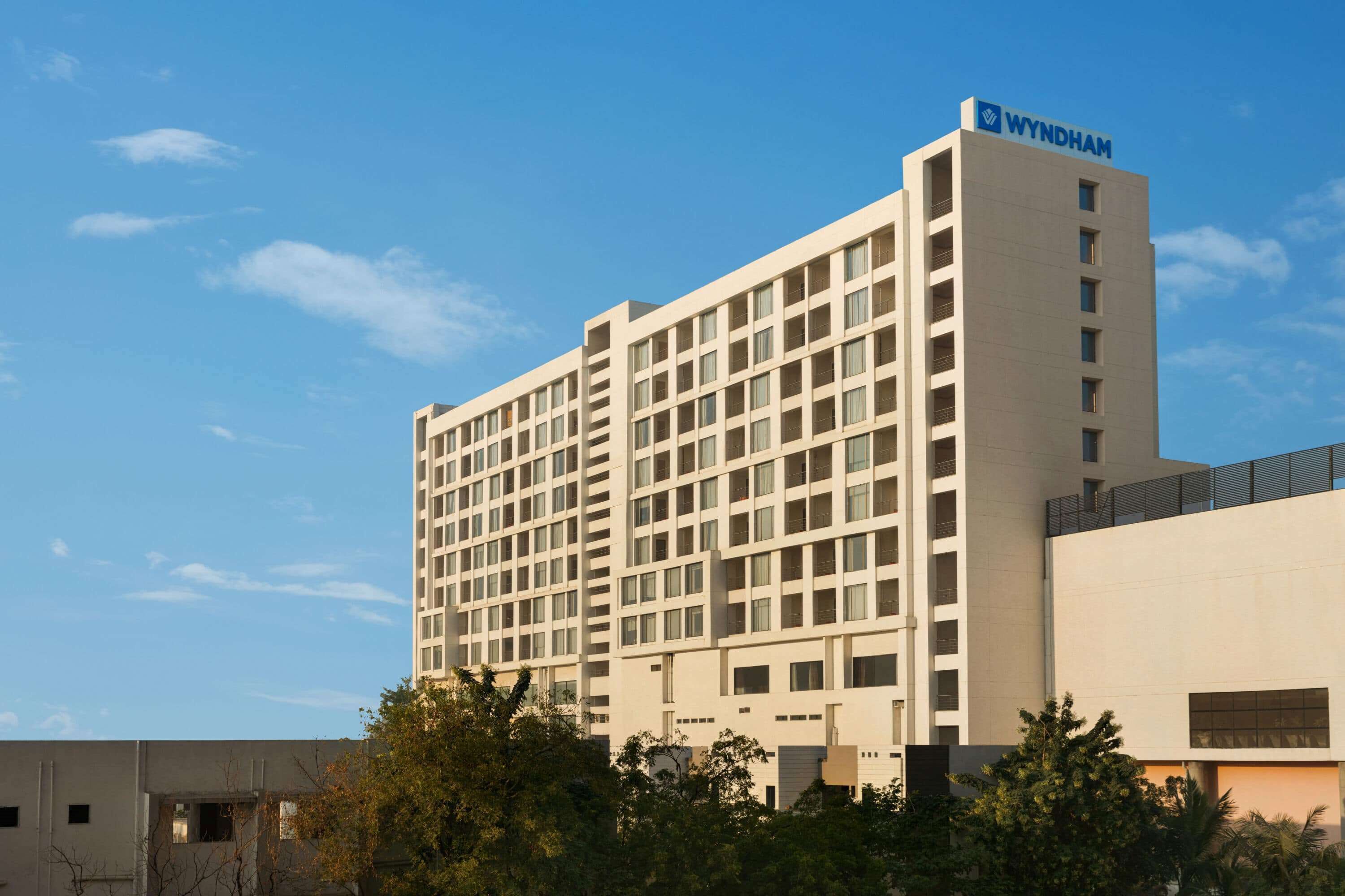 Un hotel de varios pisos con diseño moderno, que destaca un letrero grande de 'WYNDHAM' en la parte superior.