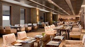 A spacious hotel dining area with multiple tables and chairs, large windows, and a modern ceiling design. - Wyndham Ahmedabad Shela (Sanand)