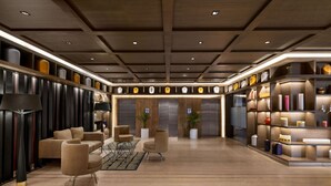 A spacious lobby with a modern design, featuring a central seating area with sofas and armchairs, a large bookshelf with decorative items, and a wooden ceiling with recessed lighting. - Wyndham Ahmedabad Shela (Sanand)