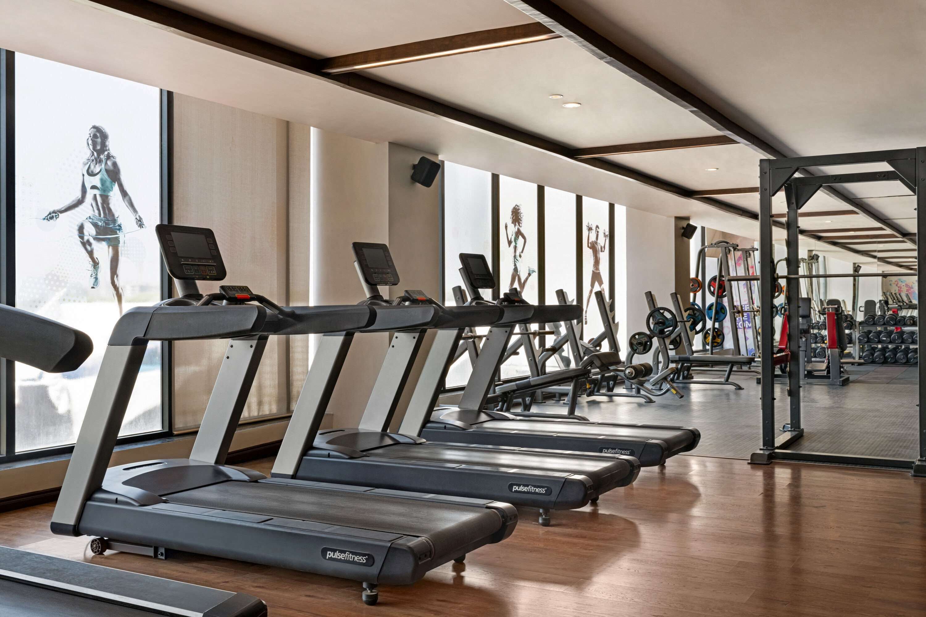 Una palestra con diverse tapis roulant, attrezzature per sollevamento pesi e ampie finestre.
