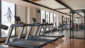Una palestra con diverse tapis roulant, attrezzature per sollevamento pesi e ampie finestre.