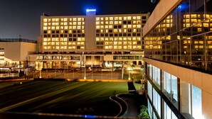 A modern hotel with multiple floors, large windows, and a well-lit facade at night. - Wyndham Ahmedabad Shela (Sanand)