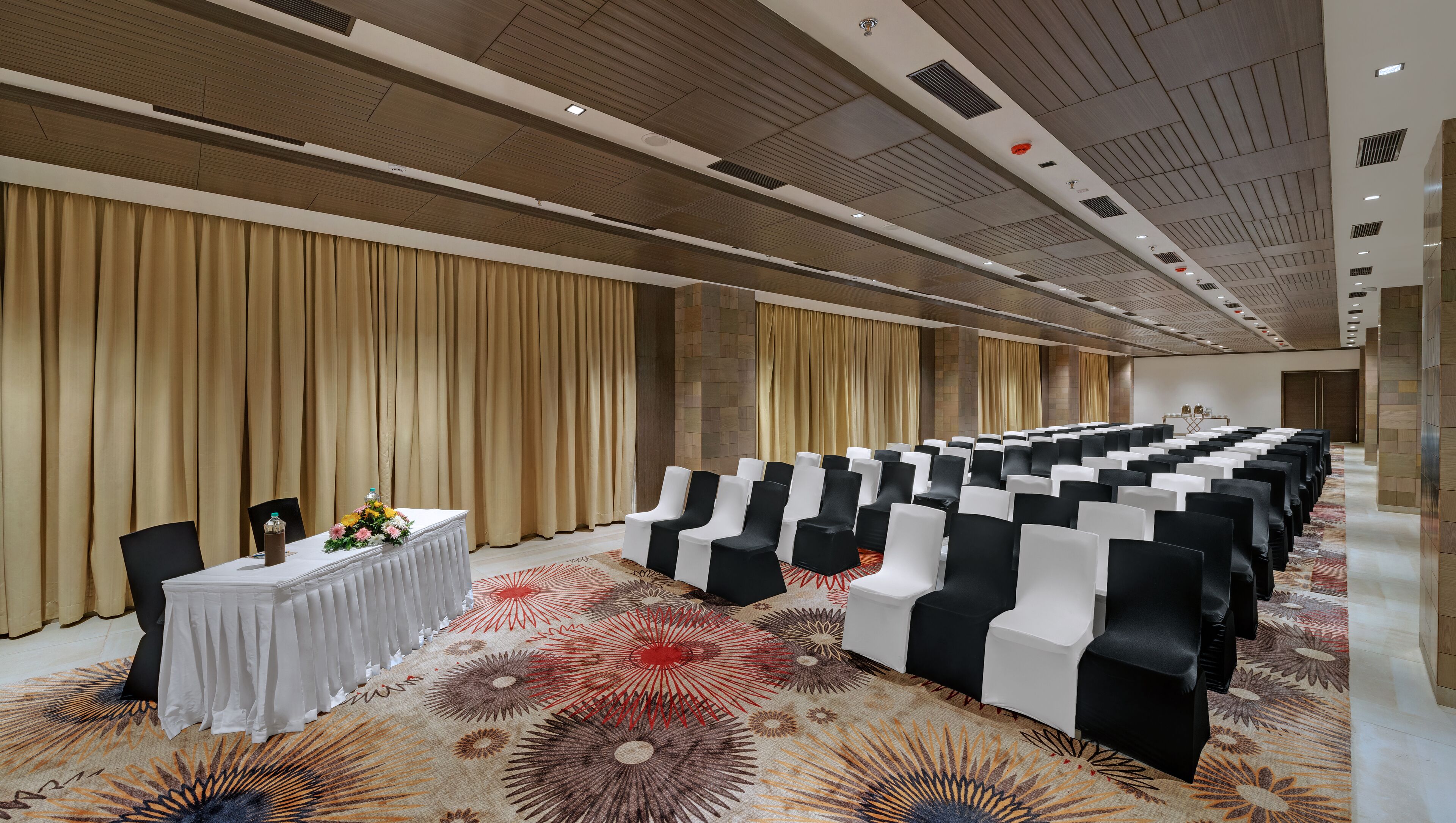 A conference room with rows of chairs, a table with a floral arrangement, and a patterned carpet.