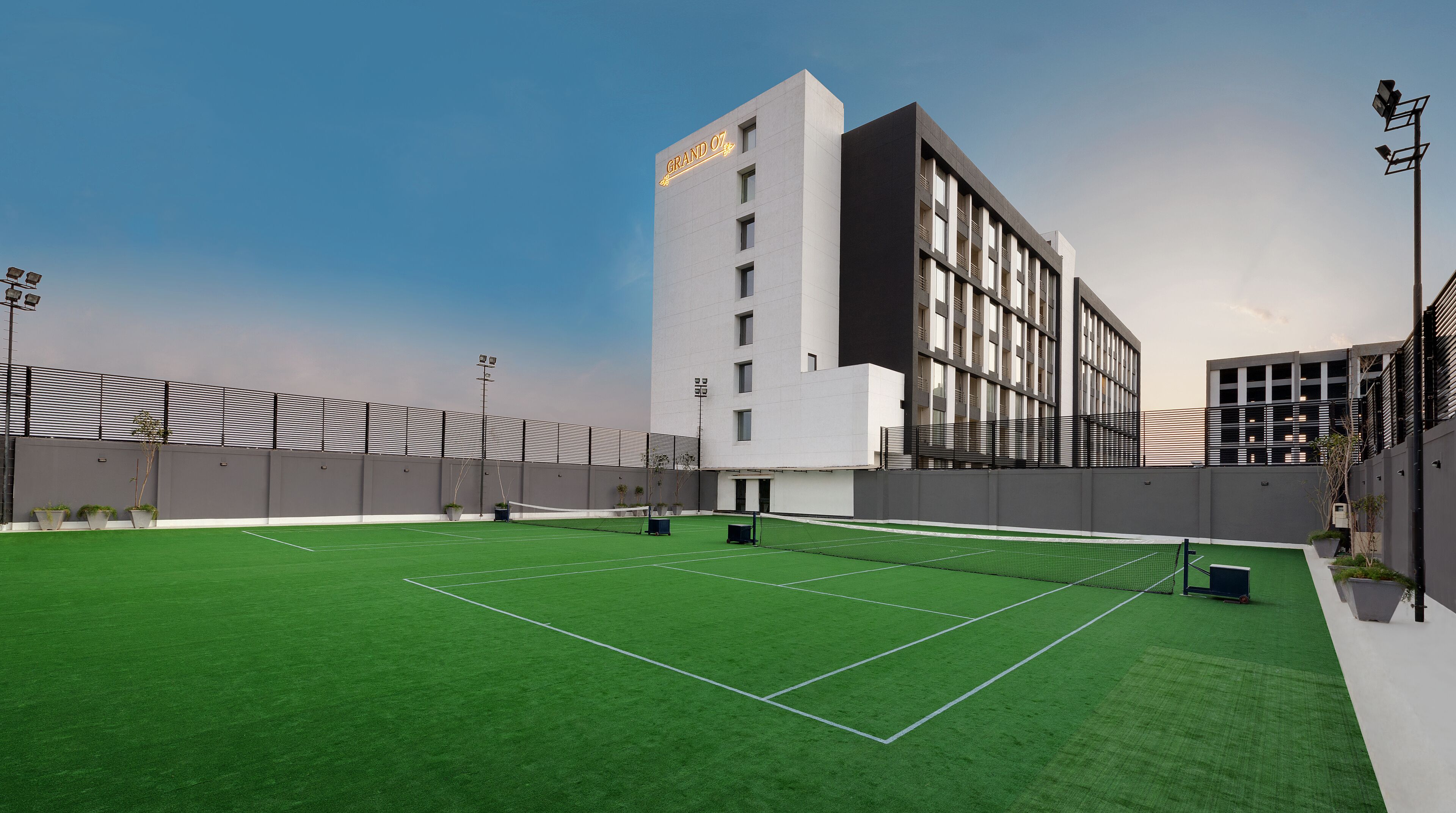 A modern building with a sign reading "GRAND 07" and a tennis court in front.