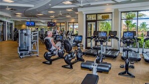 A gym with various exercise machines, a television, and large windows with a view of palm trees. - Treviso Bay Condo on rarely available Top Floor (Naples)