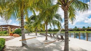 A hammock between palm trees on a sandy beach with a pool in the background. - Treviso Bay Condo on rarely available Top Floor (Naples)