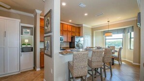 A spacious kitchen with a dining area, featuring a large island, wooden cabinets, and a view of the outdoors. - Treviso Bay Condo on rarely available Top Floor (Naples)