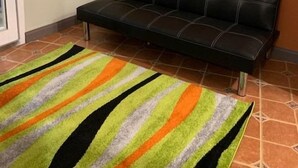 A room with a black leather sofa, a striped rug, and a framed picture on the wall.