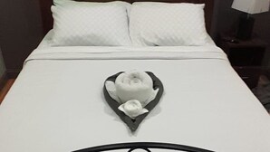 A bed with a heart-shaped towel arrangement, a wooden headboard, and a tiled floor.