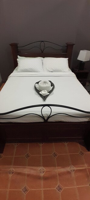 A bed with a heart-shaped towel arrangement, a wooden headboard, and a tiled floor.
