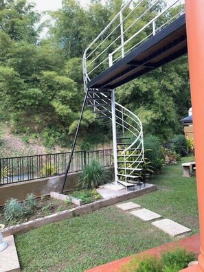 A spiral staircase leading to a bridge over a water feature, surrounded by greenery.