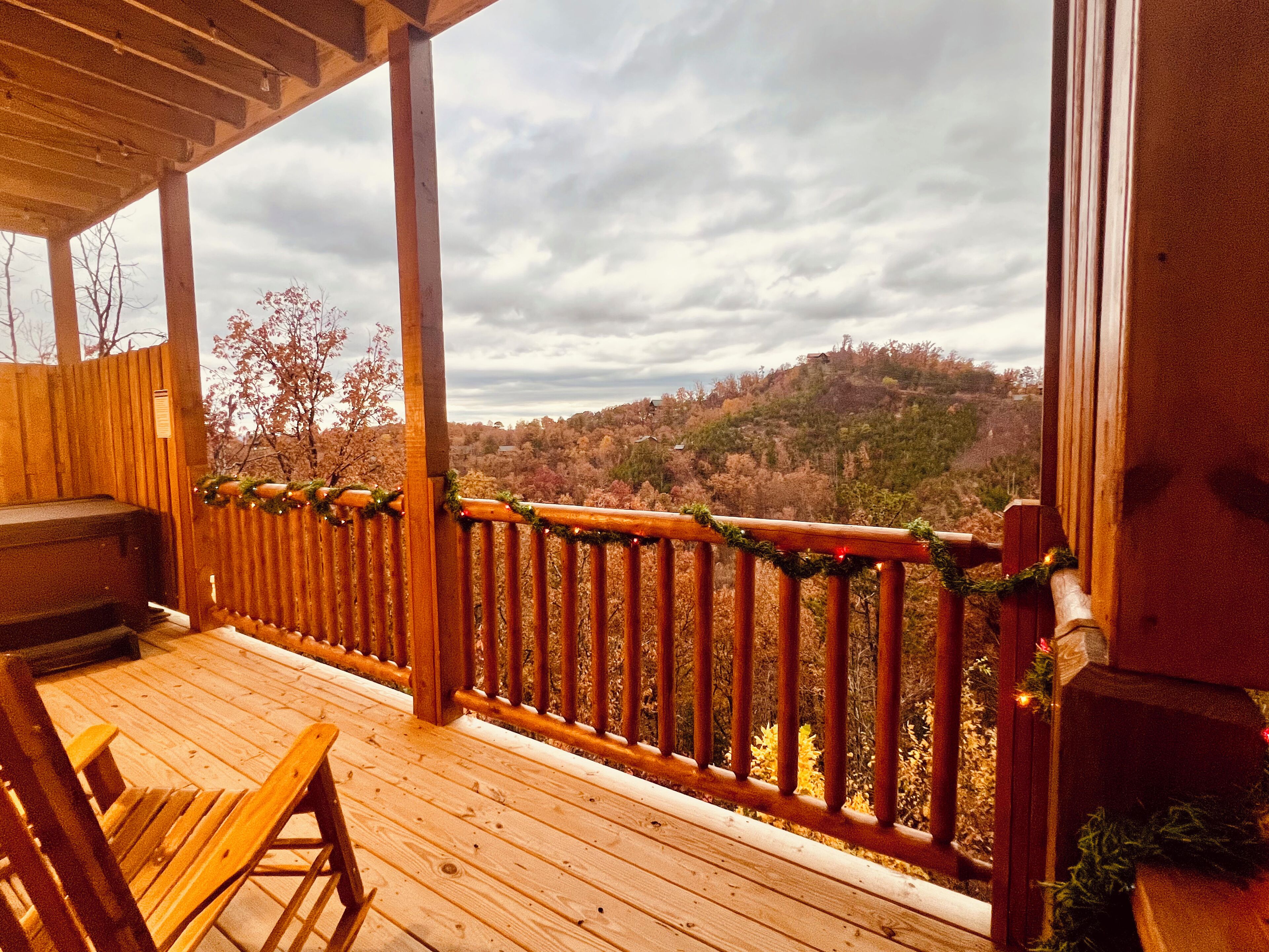 A wooden deck with a railing, a bench, and a view of a forested hillside.