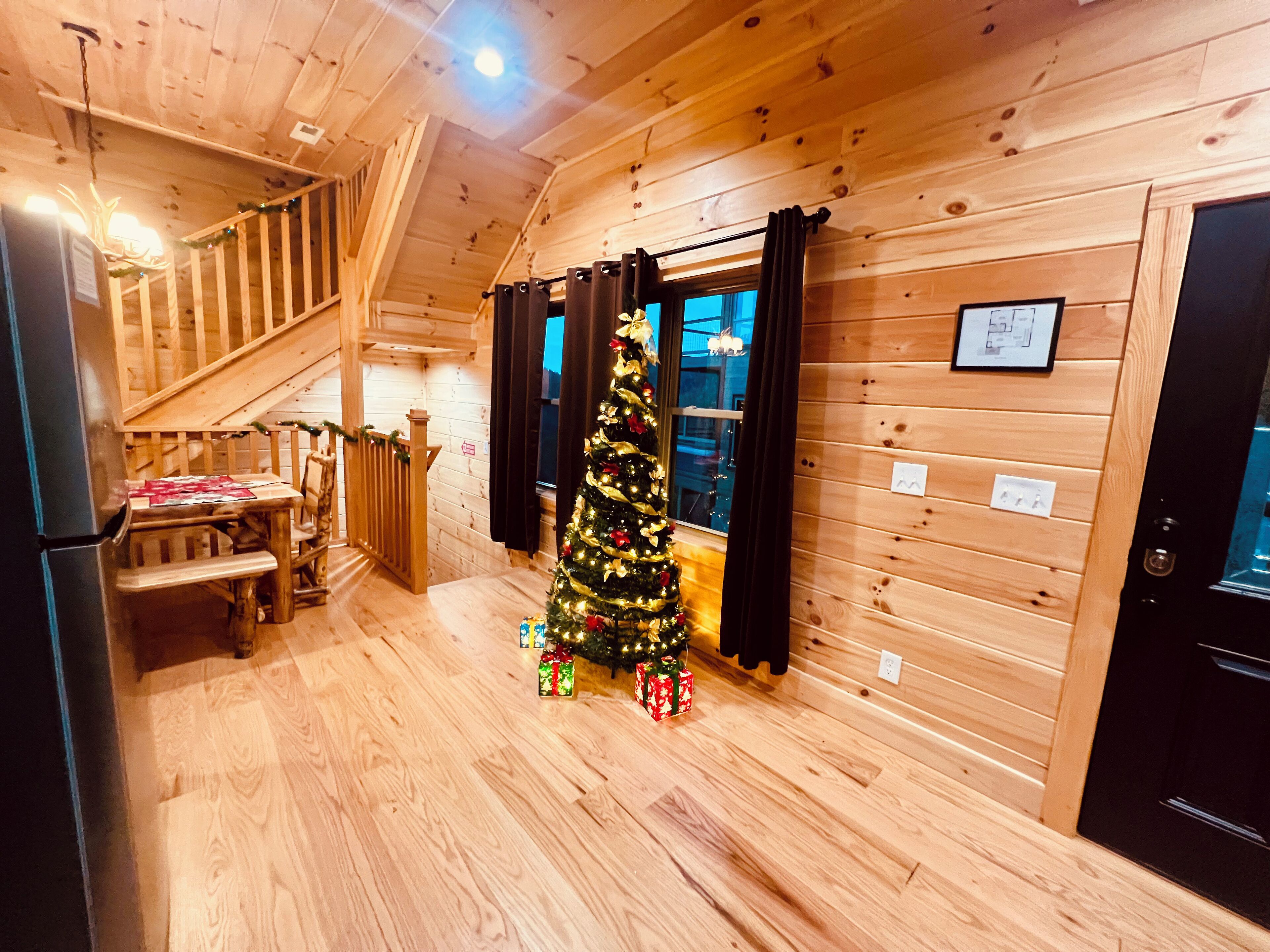 A wooden interior with a staircase, a Christmas tree, and a dining area.