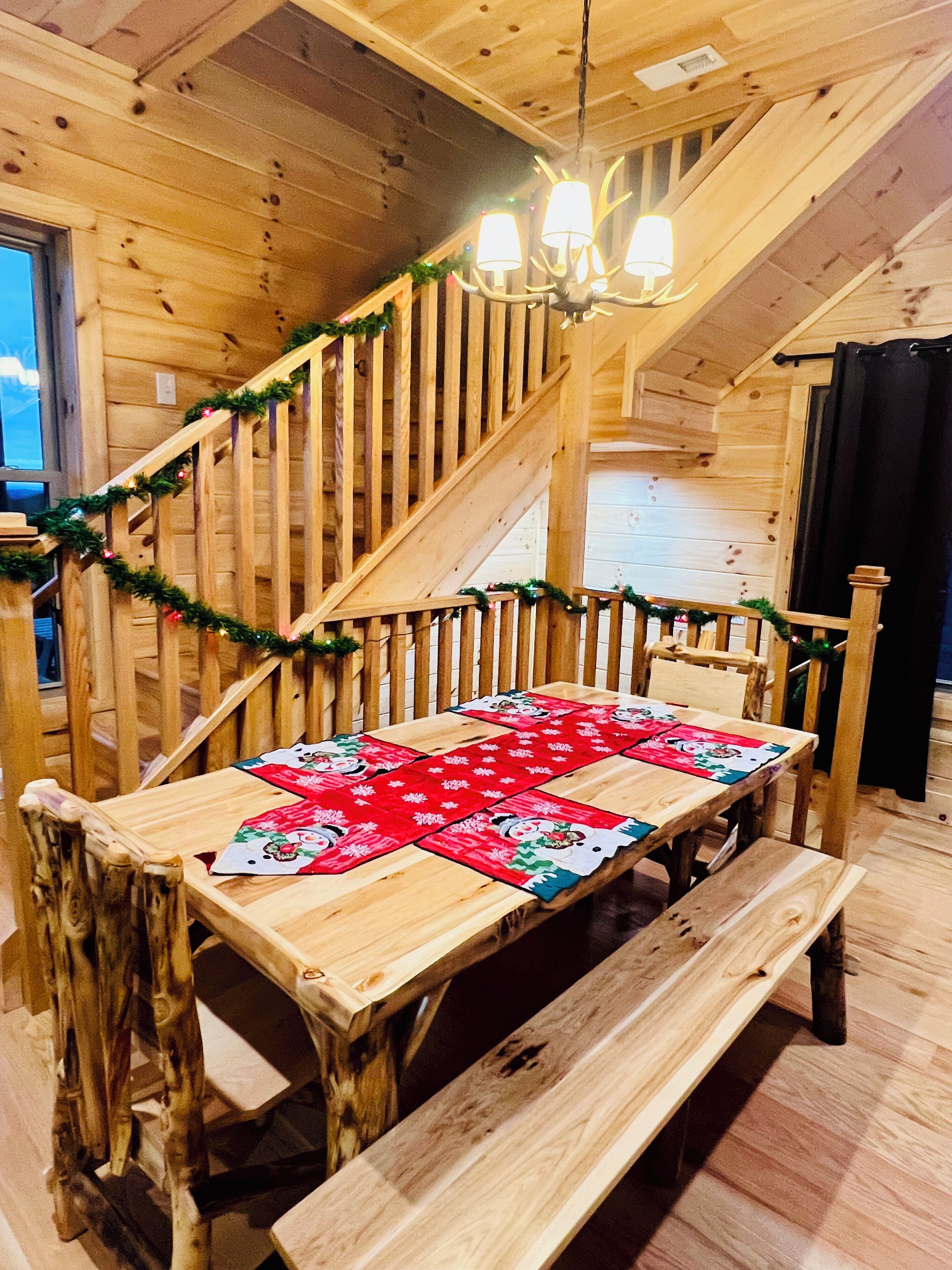 Un intérieur en bois avec un escalier, un banc et une table recouverte d’un chemin de table rouge.