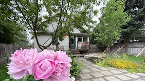 Un jardin agrémenté de pivoines et un chemin de pierre menant à une maison dotée d’un porche.