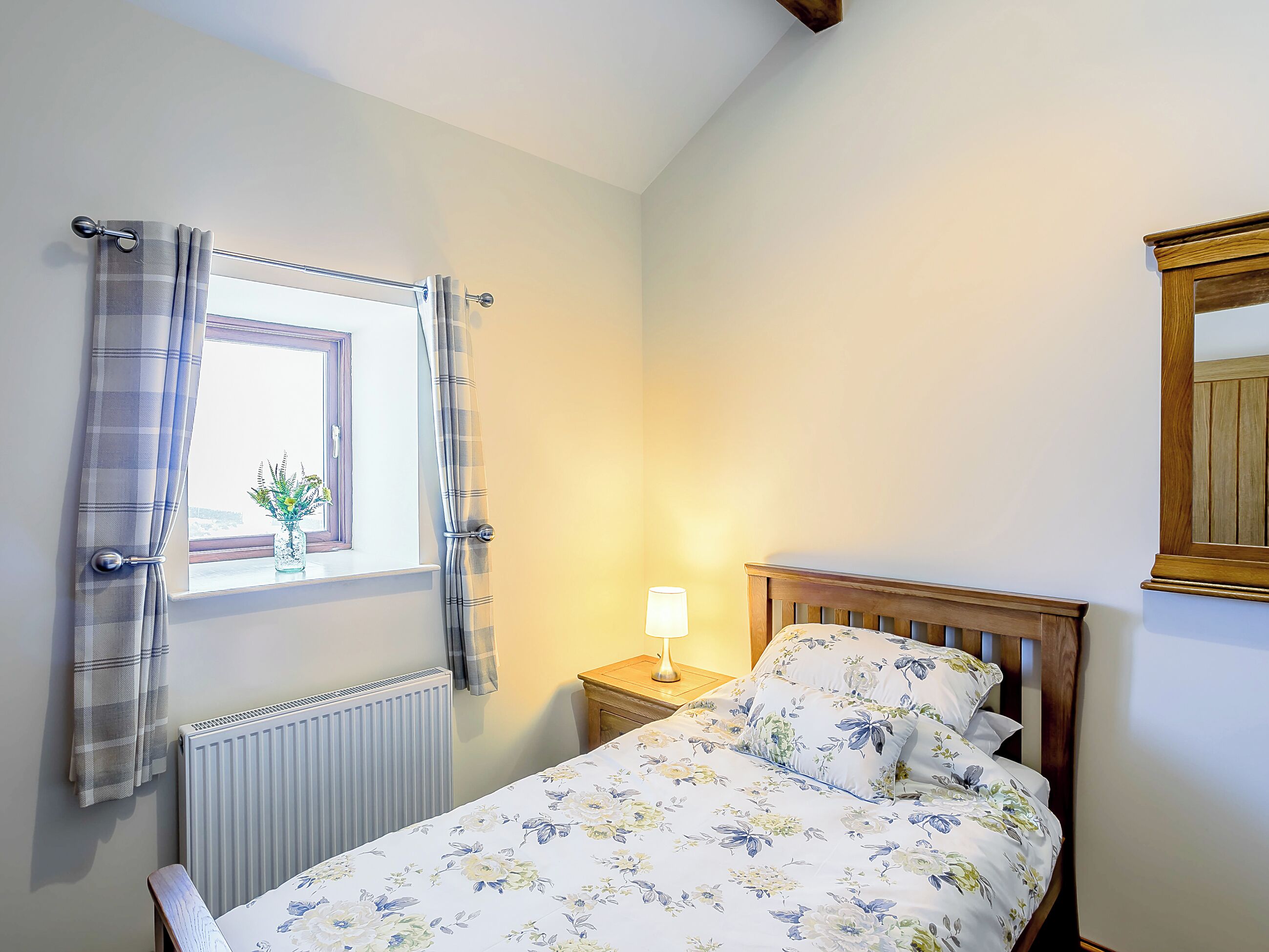 Une chambre à coucher avec un lit, une table de chevet avec une lampe, une fenêtre avec des rideaux et un radiateur.