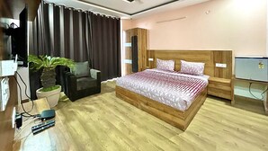 A bedroom with a bed, a chair, a desk with a plant, a ceiling fan, and a small refrigerator.