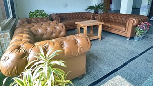 A living room with a brown leather sectional sofa, a wooden coffee table, and potted plants.