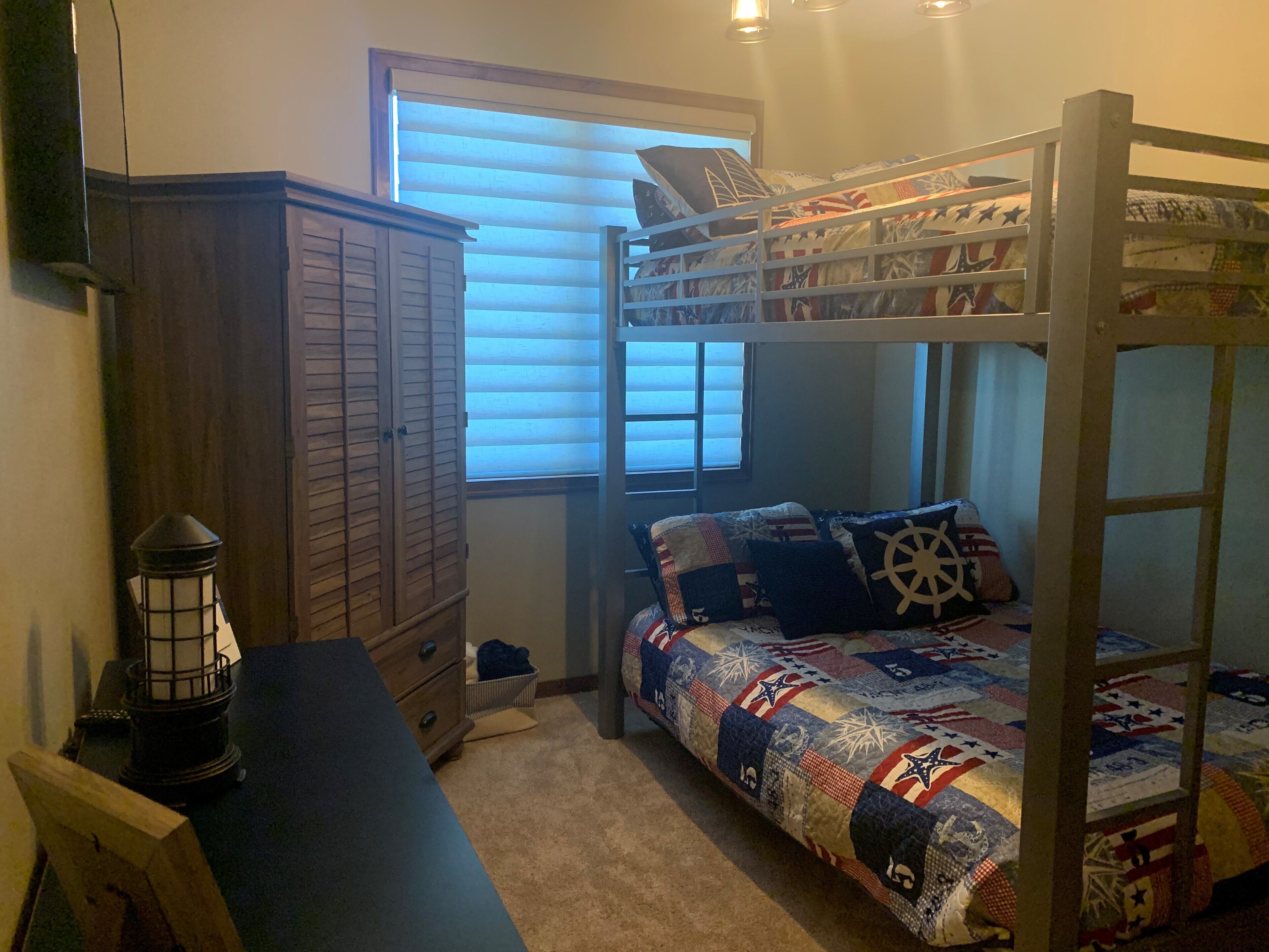 Un lit superposé avec une tête de lit matelassée, une armoire en bois et un bureau avec une lampe.