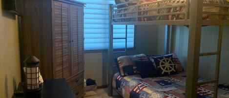 Un lit superposé avec une tête de lit matelassée, une armoire en bois et un bureau avec une lampe.