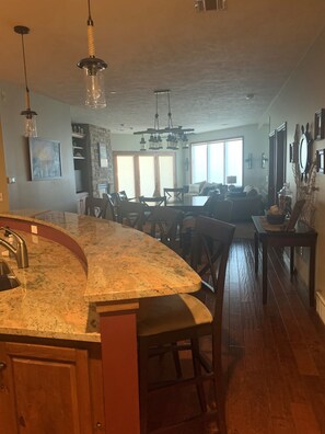 A kitchen with a curved granite countertop, wooden cabinets, and a built-in sink. There is a dining area with a table and chairs, and a large window providing natural light.