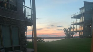 Een terras met een vuurkuil, buitenmeubilair en uitzicht op een wateroppervlak tijdens zonsondergang.
