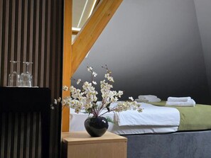 Habitació d'hotel amb llit, una taula de nit amb un vas de flors i una porta de fusta.