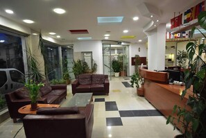 Un espace d’accueil avec un sol à carreaux, des canapés en cuir, un comptoir d’accueil et des plantes en pot.