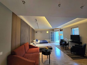 Habitació d'hotel moderna amb sofà, llit, televisió i zona de menjador.