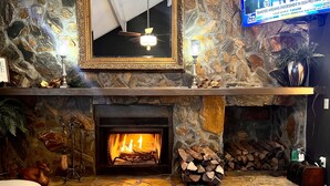 Une cheminée en pierre avec un feu de bois, un téléviseur fixé au mur et un miroir encadré au-dessus.