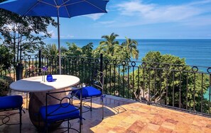 A terrace with a table and chairs, a blue umbrella, and a view of the ocean. - Beautiful Private Villa Beachfront Location, Full Staff & transfers included (Puerto Vallarta)