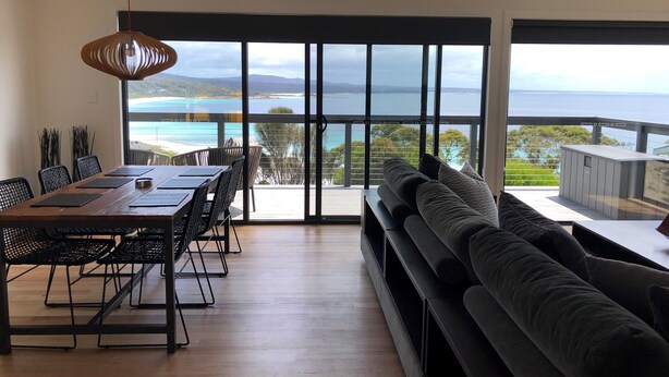 A modern living room with a large sliding glass door leading to a balcony with a view of the sea and mountains. - MOONRISE BINALONG BAY Stunning views  (Binalong Bay)