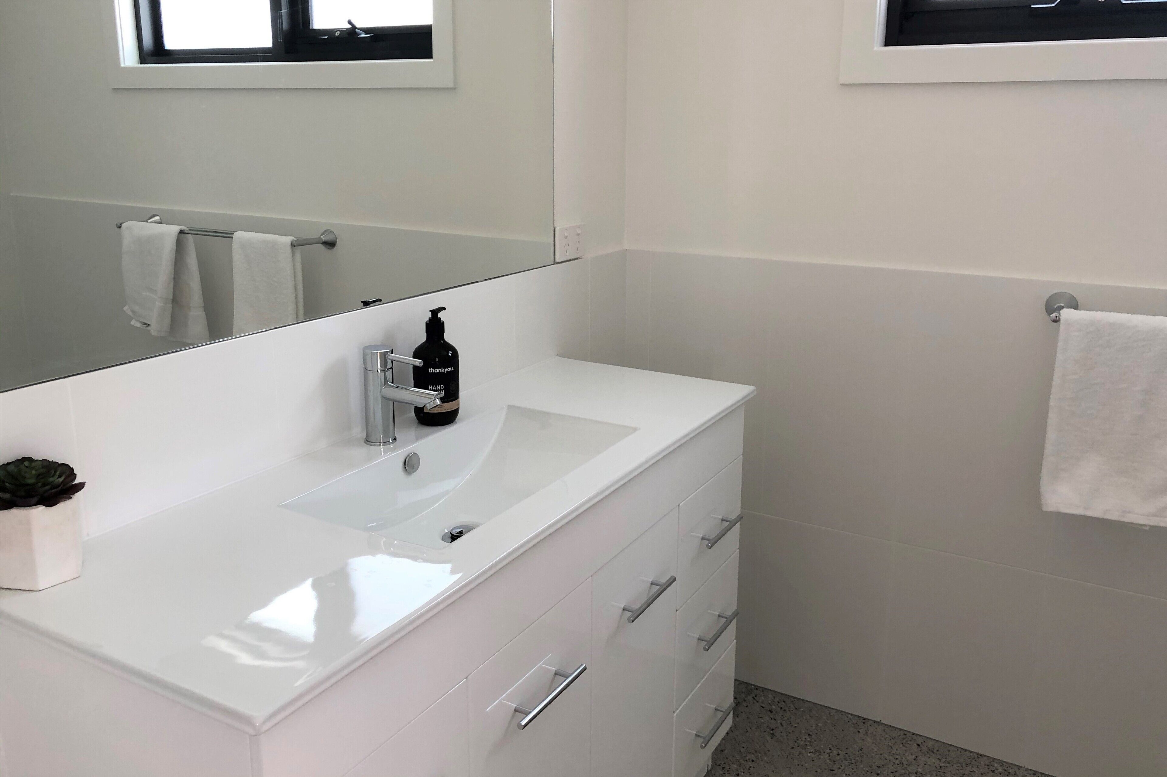 A modern bathroom with a white vanity, a large mirror, and a small plant on the counter.